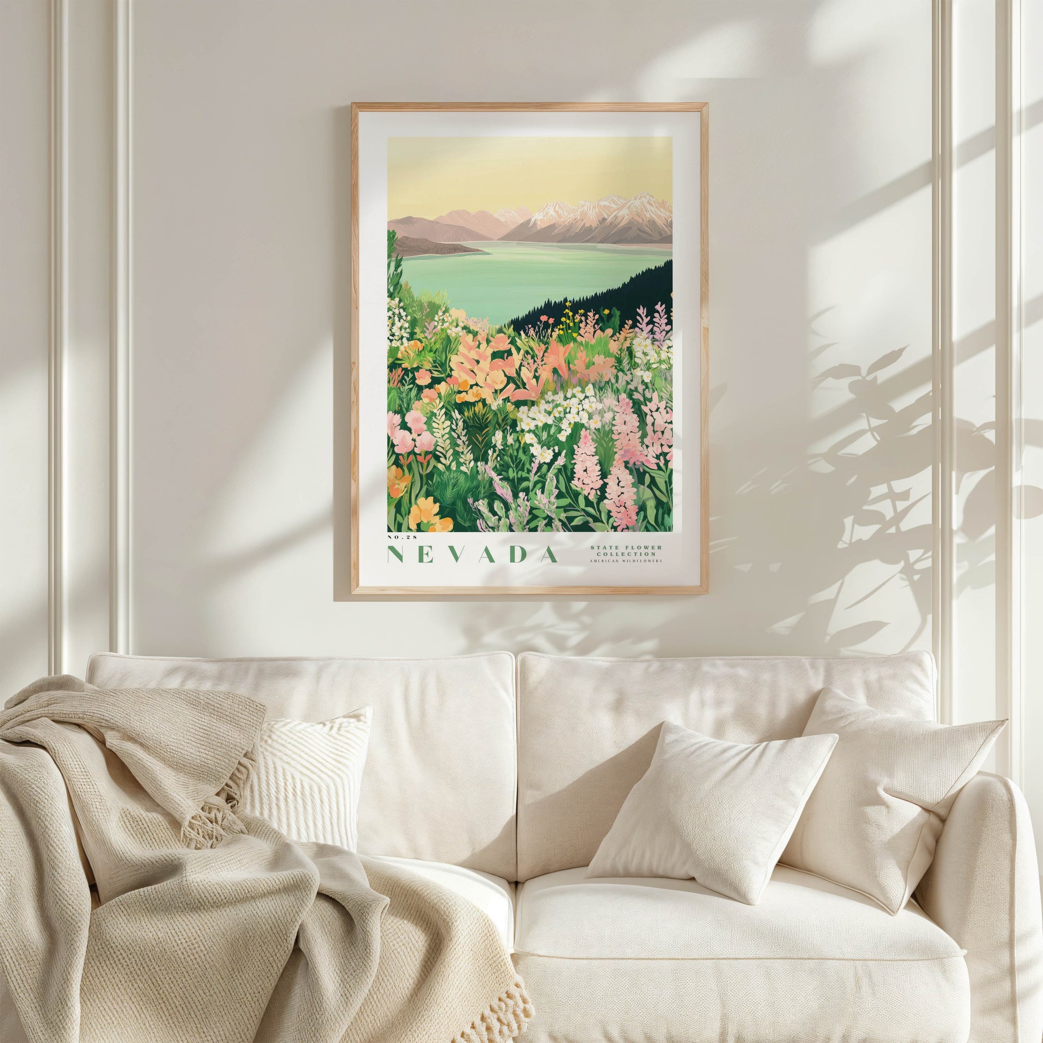 a framed poster of a scenic landscape with mountains and a lake, hanging on a wall above a white couch with a blanket draped over it.