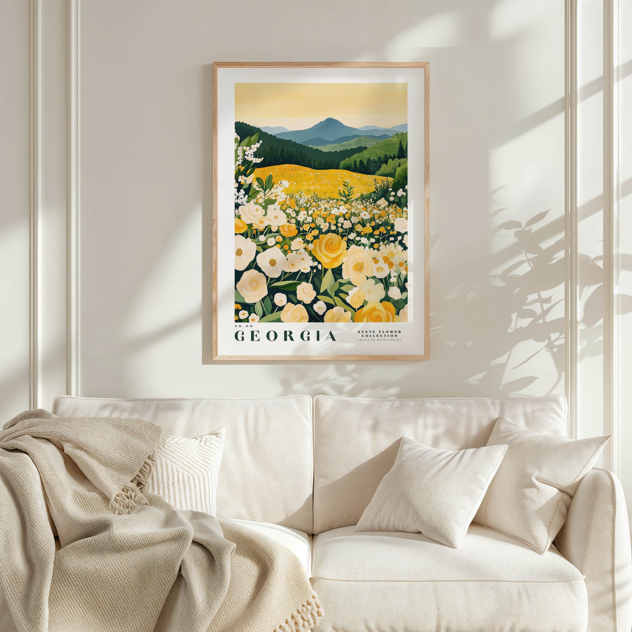 a framed poster of a field of flowers, with the word "GEORGIA" prominently displayed. The poster is hanging on a wall above a white couch, which is adorned with a blanket and pillows.
