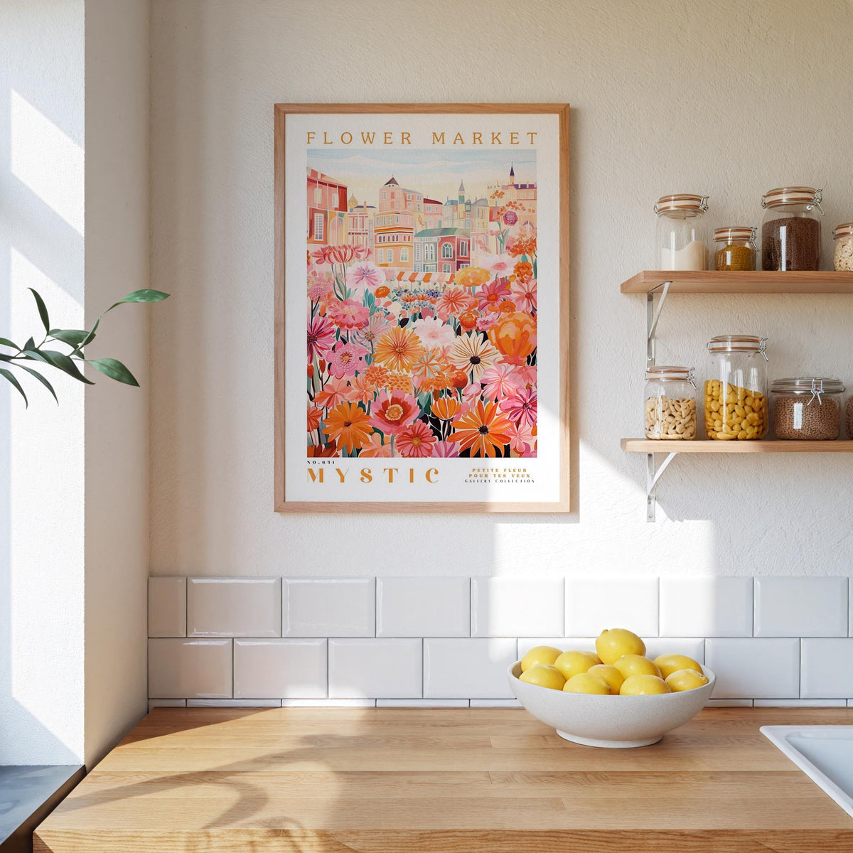 a kitchen scene with a framed poster of a colorful floral market hanging on the wall above a wooden counter. On the counter, there is a bowl of lemons and a plant. The kitchen has white tiled walls and a wooden shelf with various jars and containers.