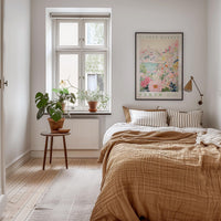 a cozy bedroom with a large bed, a nightstand with a potted plant, and a framed poster of a cityscape on the wall.