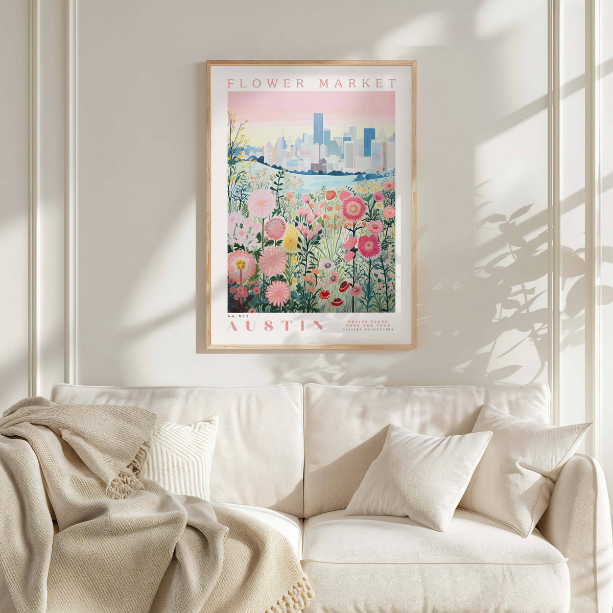 a framed poster of a cityscape with a field of flowers in the foreground, hanging on a wall above a white couch with a blanket draped over it.