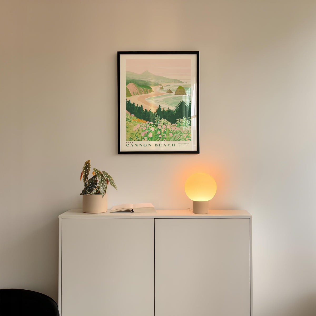 a framed poster of a scenic landscape hanging on a wall above a white cabinet with a plant and a lamp on top.