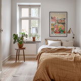 a cozy bedroom with a large bed, a nightstand with a plant, and a framed poster of a flower market in New Orleans.