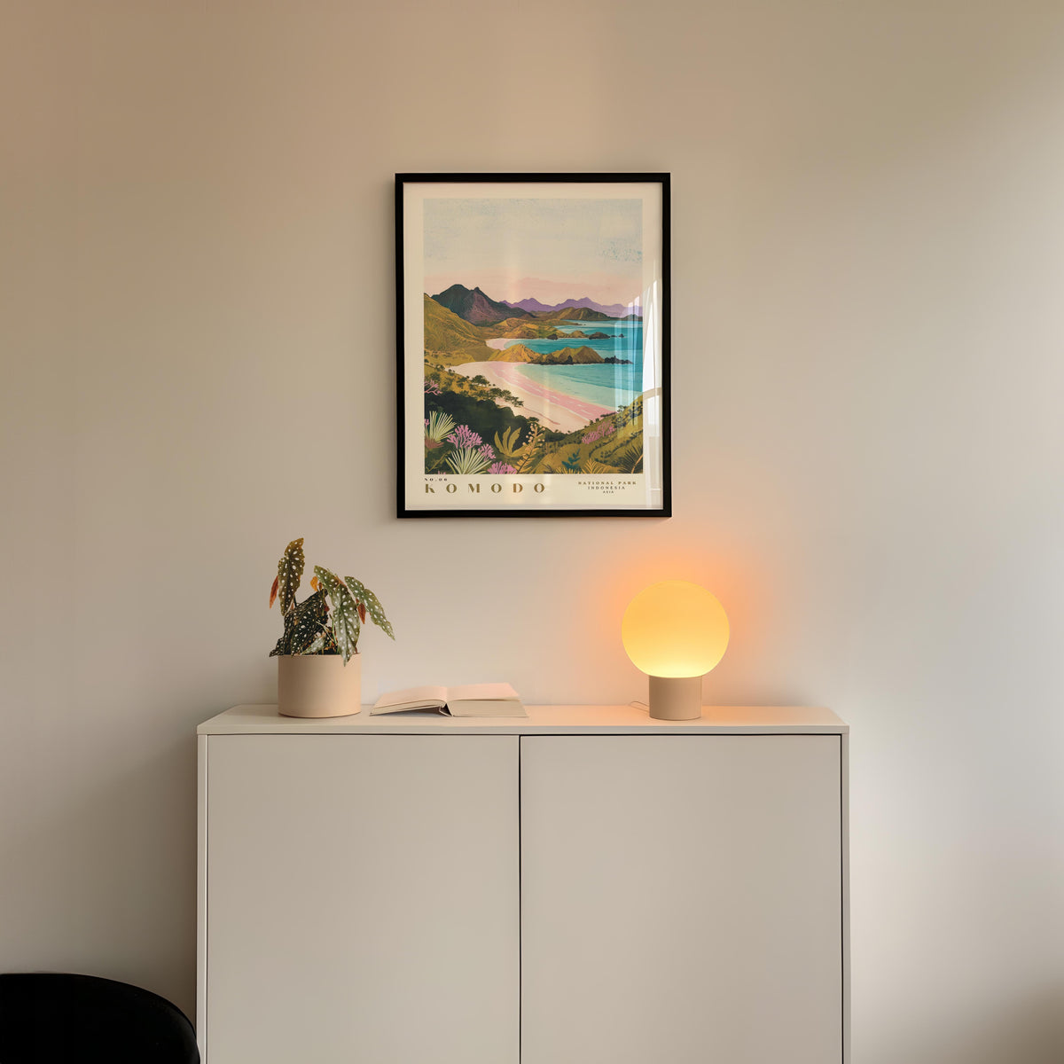 a white cabinet with a framed picture of a scenic landscape hanging above it, and a small lamp on the cabinet.