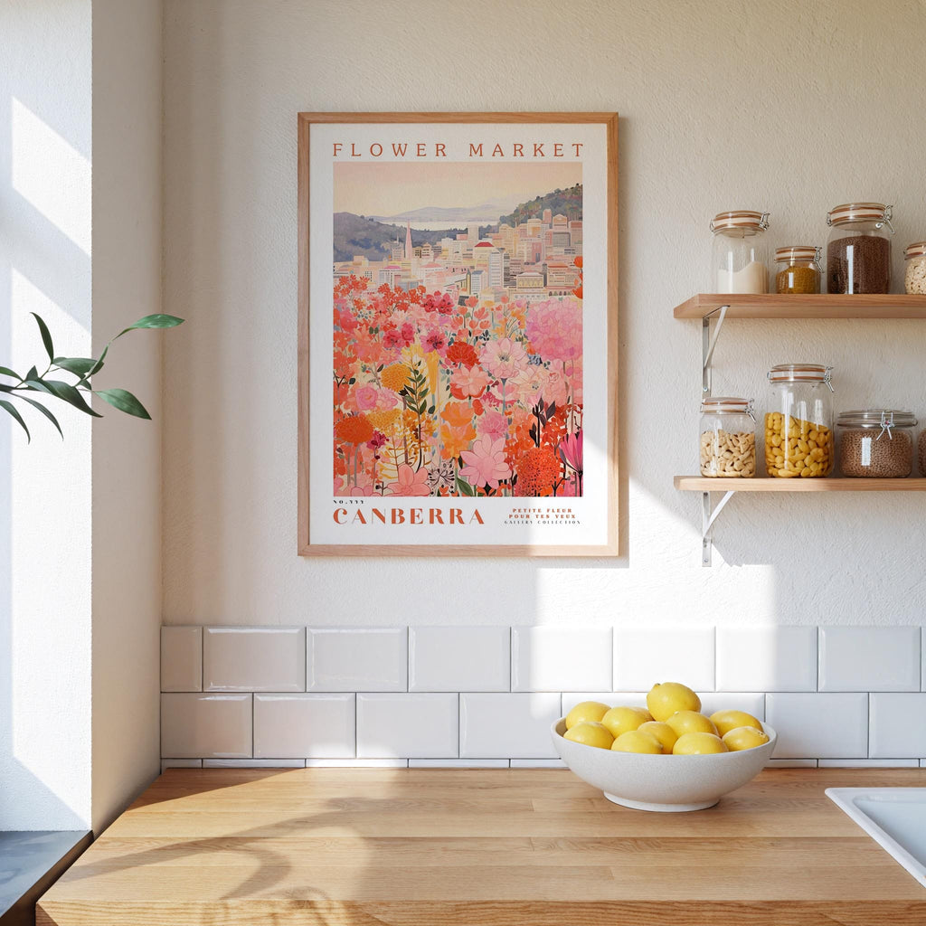 a kitchen scene with a framed poster of a flower market in Australia hanging on the wall above a wooden counter. On the counter, there is a bowl of lemons and a plant.