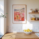 a kitchen scene with a framed poster of a flower market in Australia hanging on the wall above a wooden counter. On the counter, there is a bowl of lemons and a plant.