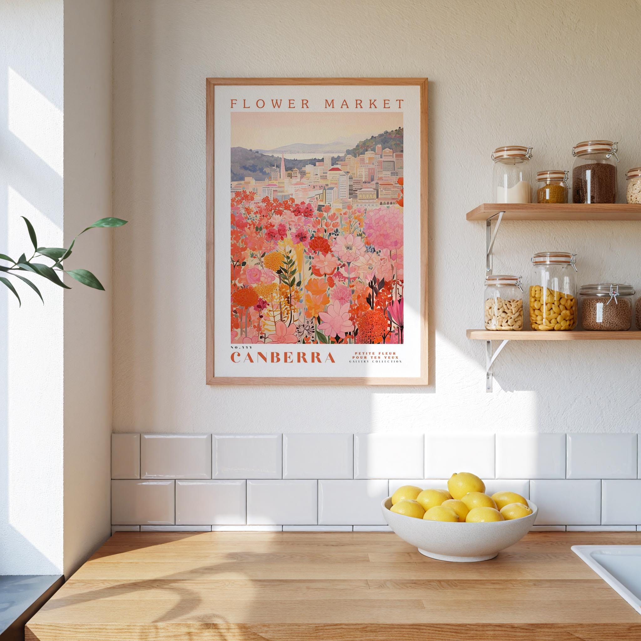 a kitchen scene with a framed poster of a flower market in Australia hanging on the wall above a wooden counter. On the counter, there is a bowl of lemons and a plant.