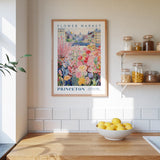a kitchen counter with a bowl of lemons, a framed poster of a flower market, and shelves with jars and containers.