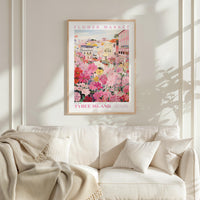 a framed poster of a colorful floral scene hanging on a wall above a white couch with a blanket draped over it.