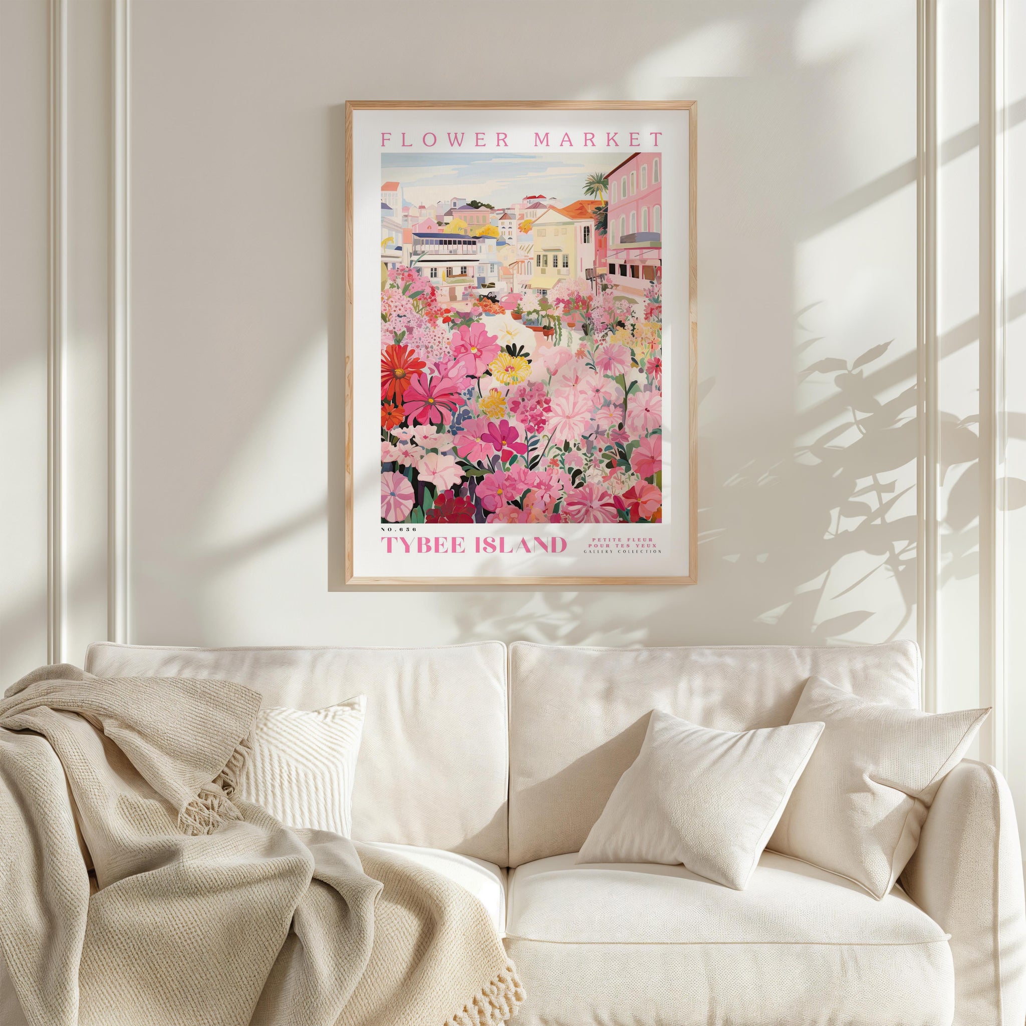 a framed poster of a colorful floral scene hanging on a wall above a white couch with a blanket draped over it.