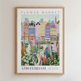 The image is a framed poster depicting a colorful and vibrant flower market in Amsterdam, with a variety of flowers and plants in the foreground and a cityscape in the background.