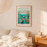 a bedroom scene with a framed poster of a flower market in San Diego hanging on the wall above a bed with striped pillows.
