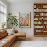 a cozy living room with a large window, a comfortable leather couch, a bookshelf filled with books, and a framed poster of a flower market on the wall.