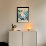 a white cabinet with a framed picture of a beach scene hanging above it, and a small lamp on the cabinet.