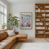 a cozy living room with a large window, a brown leather sofa, a wooden bookshelf filled with books, and a framed poster of a colorful floral scene hanging on the wall.