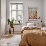 A cozy bedroom with a large bed, a nightstand with a plant, and a framed poster of the Golden Gate Bridge on the wall.