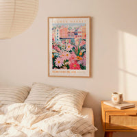 a bedroom setting with a framed poster of a colorful floral scene hanging on the wall above a bed with striped pillows.