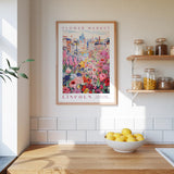 a framed poster of a colorful floral scene hanging on a wall above a wooden countertop with a bowl of lemons.