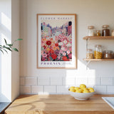 a framed poster of a cityscape with a flower market in the background, hanging on a wall above a kitchen counter with a bowl of lemons.