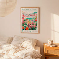 a bedroom setting with a framed poster of a colorful garden hanging on the wall above a bed with striped pillows.