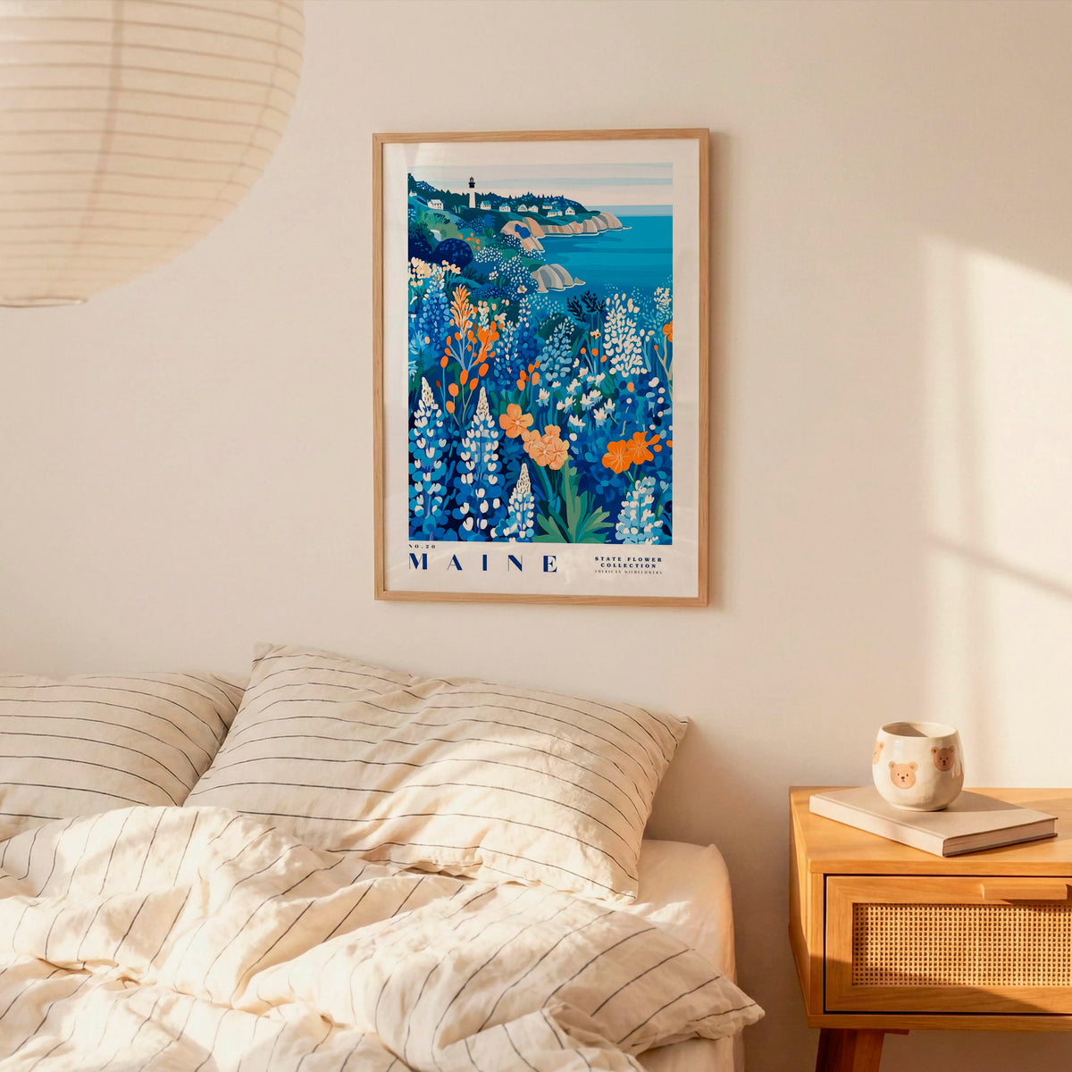 a bedroom scene with a framed poster of a coastal landscape hanging on the wall above a bed with striped pillows.