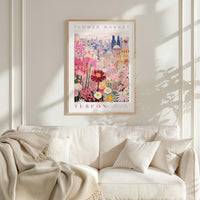a framed poster of a colorful floral scene hanging on a wall above a white couch with a blanket draped over it.