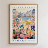 A framed poster depicting a vibrant flower market in New York City, with a variety of colorful flowers and a cityscape in the background.