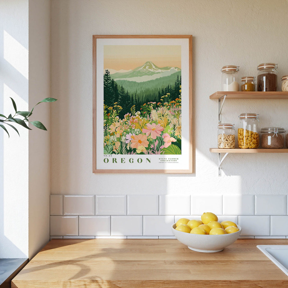 a framed poster of a mountain landscape with flowers hanging on a wall above a wooden countertop with a bowl of lemons.