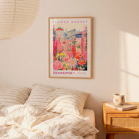 a bedroom scene with a framed poster of a colorful floral market hanging on the wall above a bed with striped pillows.