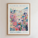 The image is a framed poster depicting a colorful and vibrant flower market in a city, with various flowers and plants in different shades of pink, blue, and green.
