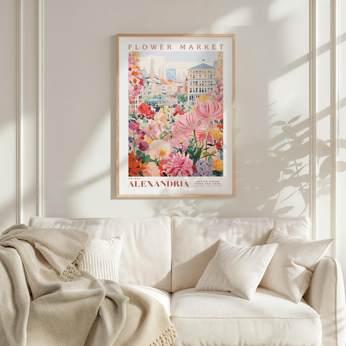 a framed poster of a colorful floral scene hanging on a wall above a white couch with a blanket draped over it.