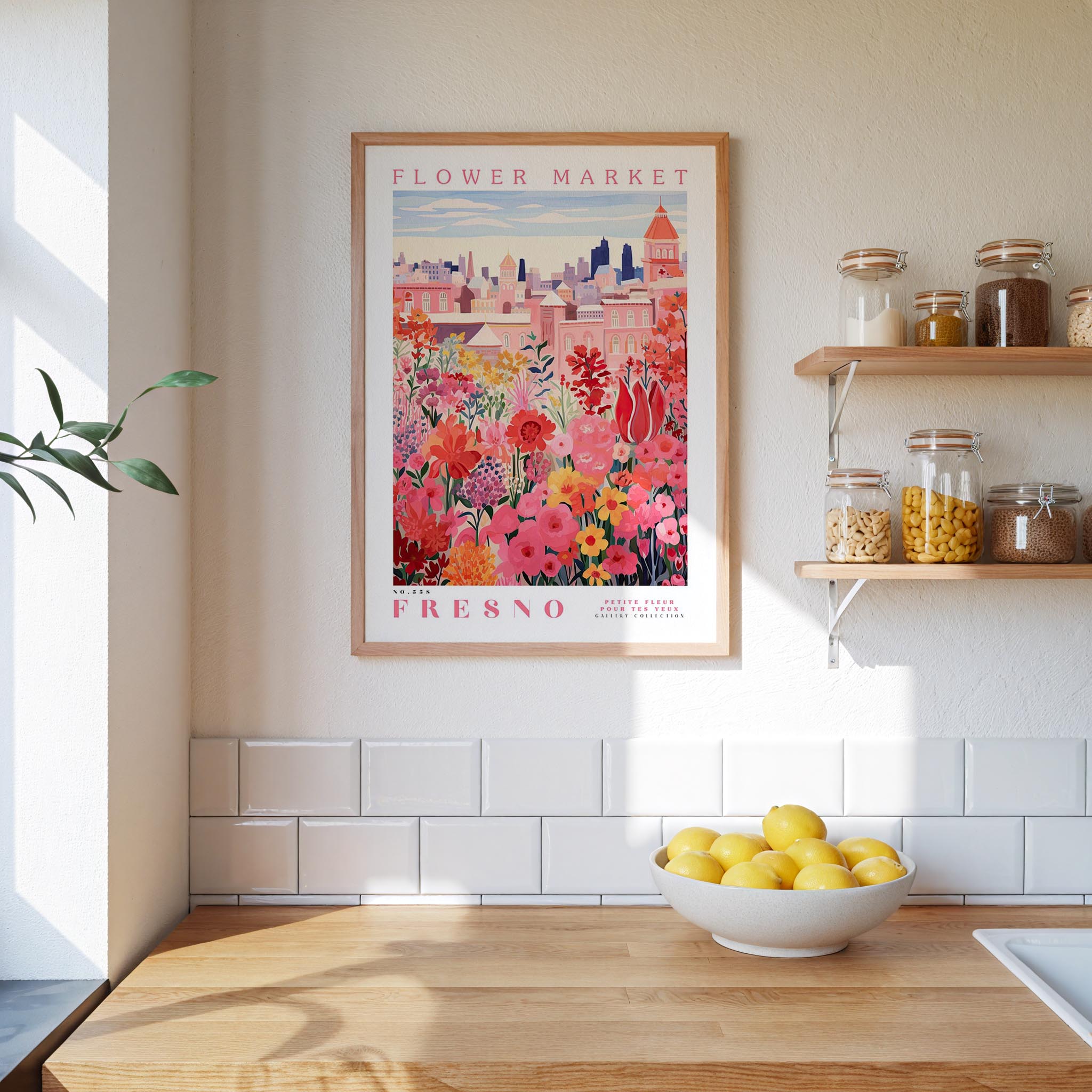 a framed poster of a colorful floral scene hanging on a wall above a kitchen counter with a bowl of lemons on it.