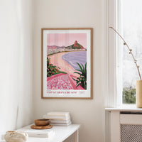 a framed poster of Copacabana Beach hanging on a wall, with a white table and a plant in the foreground.