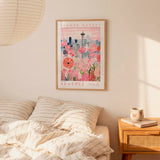 a framed poster of a cityscape with a flower market in the background, hanging on a wall above a bed with striped pillows.