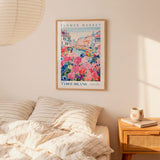 a bedroom scene with a framed poster of a flower market hanging on the wall above a bed with striped pillows.