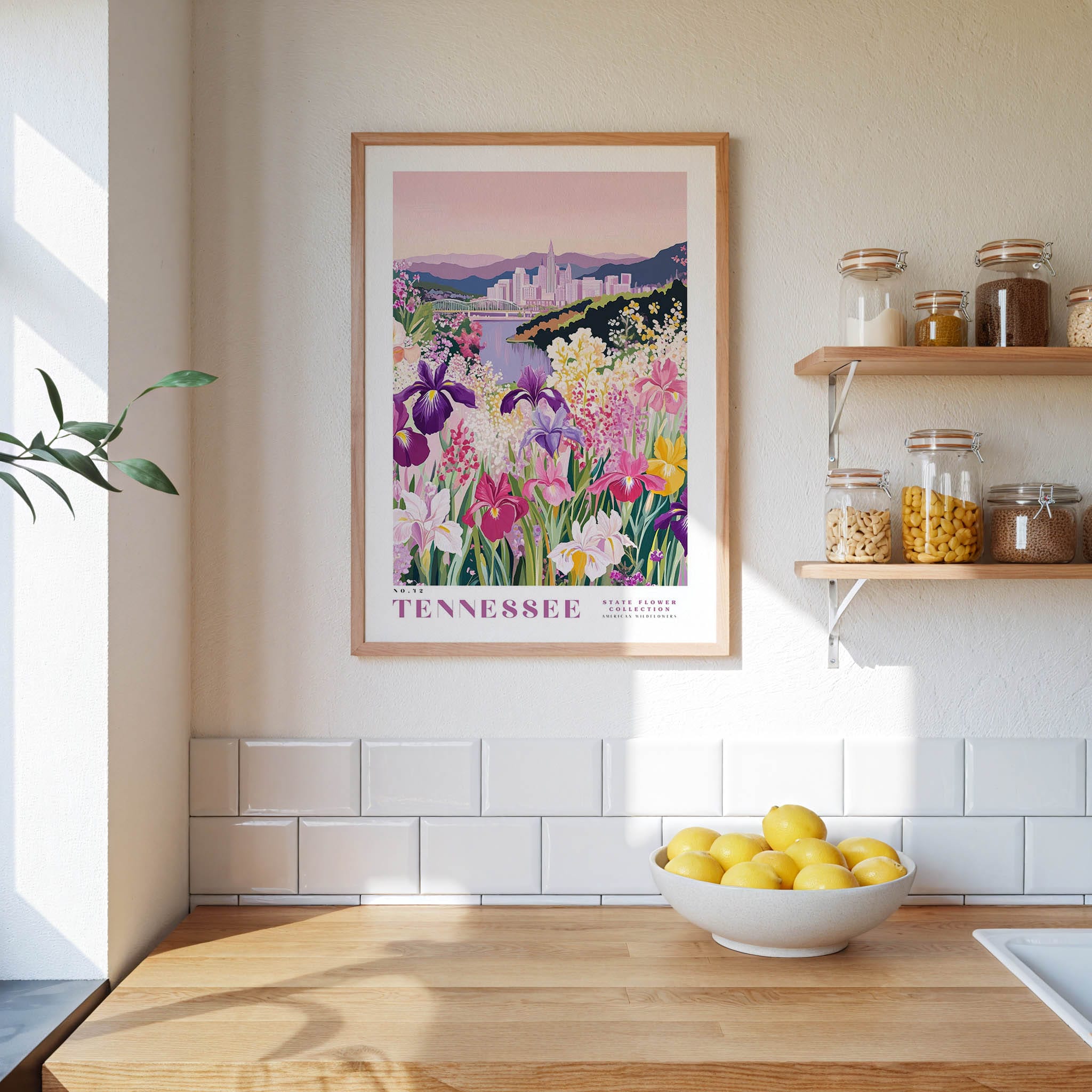 a framed poster of a colorful garden scene with flowers, hanging on a wall above a wooden countertop with a bowl of lemons.