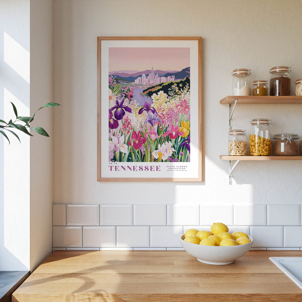 a framed poster of a colorful garden scene with flowers, hanging on a wall above a wooden countertop with a bowl of lemons.