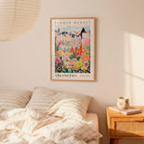 a bedroom setting with a framed poster of a colorful garden hanging on the wall above a bed with striped pillows.