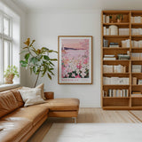 a cozy living room with a large window, a comfortable leather sofa, a wooden bookshelf filled with books, and a framed poster of a flowery landscape hanging on the wall.