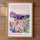 The image is a framed poster depicting a vibrant field of colorful wildflowers, with mountains in the background.