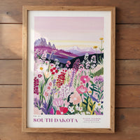 The image is a framed poster depicting a vibrant field of colorful wildflowers, with mountains in the background.