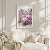 a framed poster of a cityscape with a flower market in the background, hanging on a wall above a white couch with a blanket draped over it.