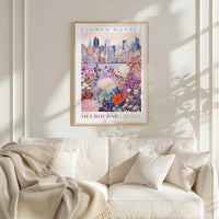a framed poster of a cityscape with a flower market in the background, hanging on a wall above a white couch with a blanket draped over it.