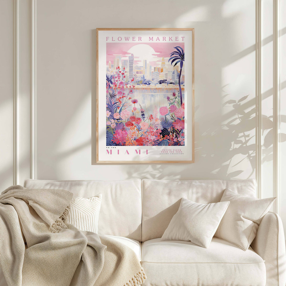 a poster of a flower market in Miami hanging on a wall above a white couch with a blanket draped over it.