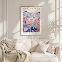 a framed poster of a colorful floral scene hanging on a wall above a white couch with pillows.