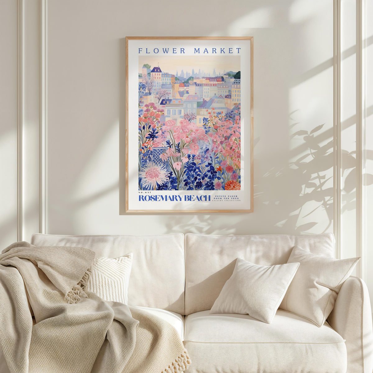 a framed poster of a colorful floral scene hanging on a wall above a white couch with pillows.