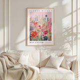 a framed poster of a cityscape with a colorful floral design, hanging on a wall above a white couch with a blanket draped over it.