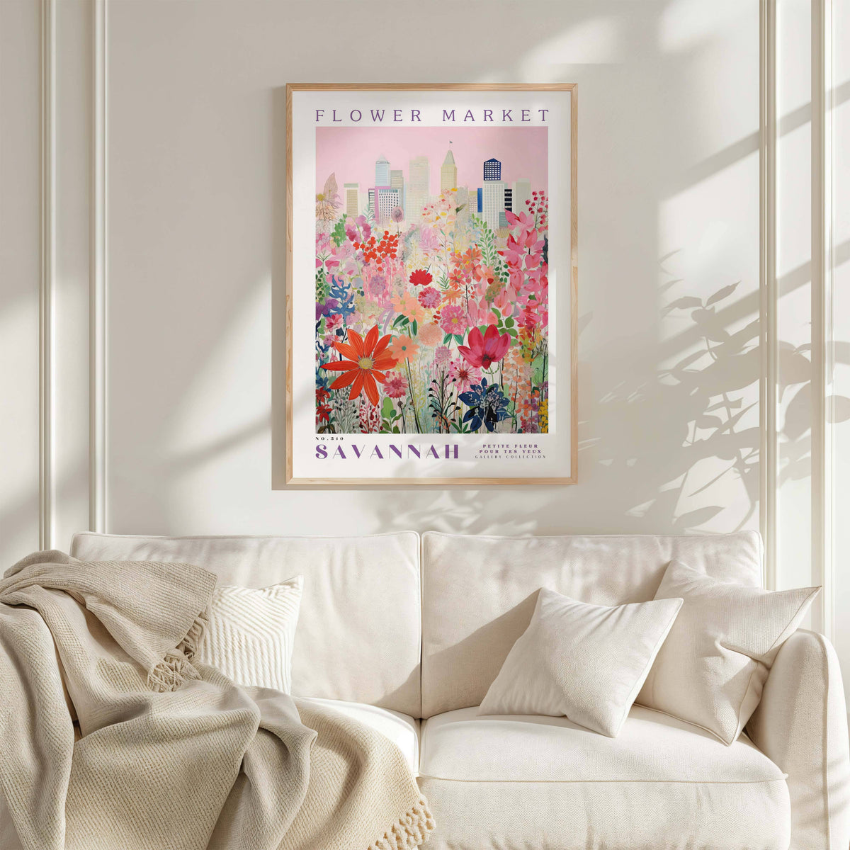 a framed poster of a cityscape with a colorful floral design, hanging on a wall above a white couch with a blanket draped over it.