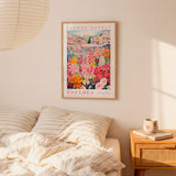 a bedroom scene with a framed poster of a colorful garden hanging on the wall above a bed with striped pillows.