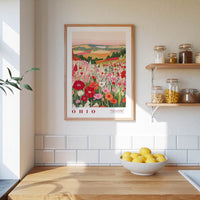 a kitchen counter with a bowl of lemons, a framed poster of a field of flowers, and a shelf with jars and containers.